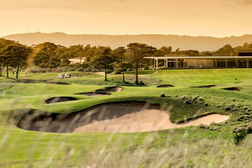 Rolling green hills of golf course with bunkers, golf carts and clubhouse