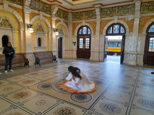 A woman in a gold-braided dress swoons on the mosaic floor of the ornate booking hall of Dunedin Railway Station.