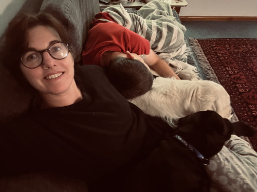 A picture of Sarah with her son and the two dogs cuddled up on the couch.